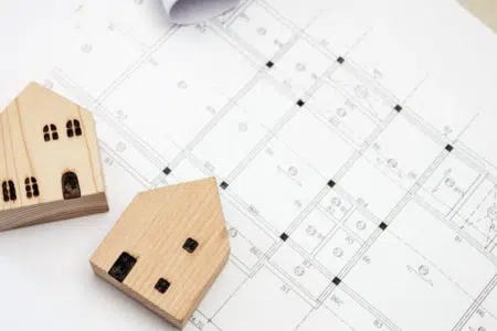 plany mieszkań rozłożone na blacie i drewniane figurki domów jednorodzinnych