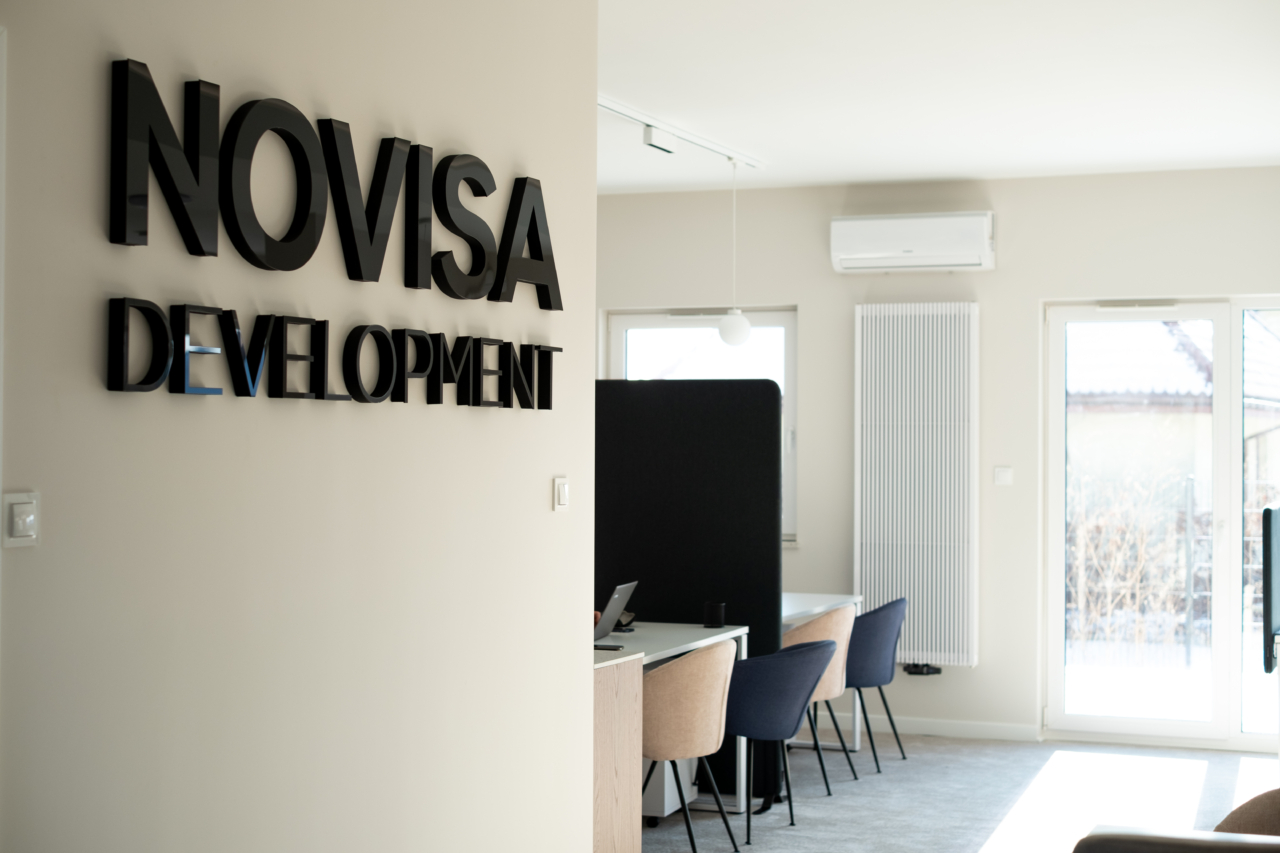 wnętrze biura sprzedaży duże logo novisa development na ścianie i biurka do spotkań z klientami