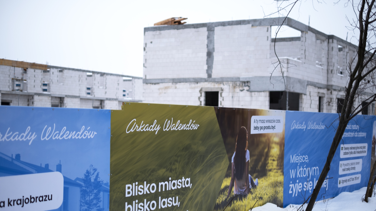 widok na budowę osiedla z ulicy z widocznym ogrodzeniem osiedla