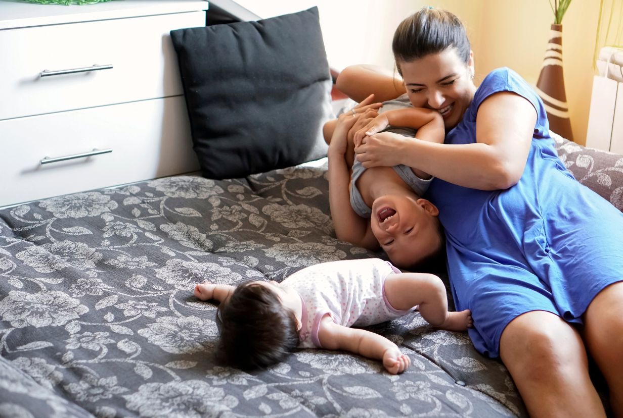 kobieta bawi się z kilkuletnim dzieckiem a obok leży niemowlak