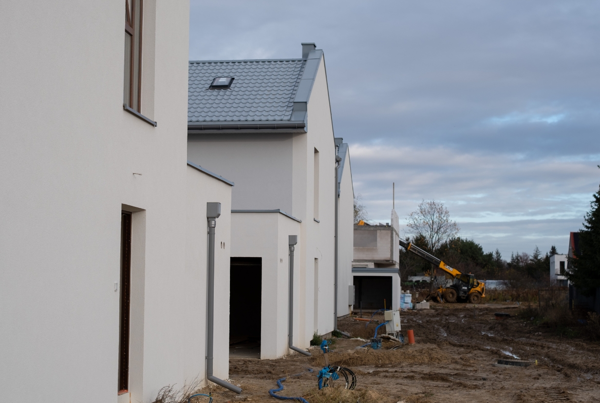 plac budowy z budynkami szeregowymi i bliźniaczymi na pierwszym planie oraz sprzęt budowlany w tle