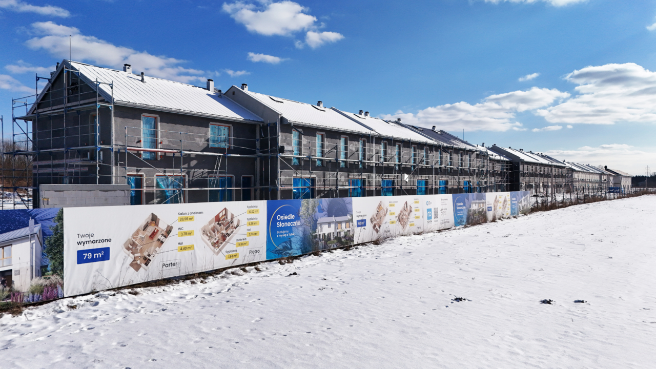 widok z oddali na budynki z gotowym ociepleniem i ogrodzenie placu budowy