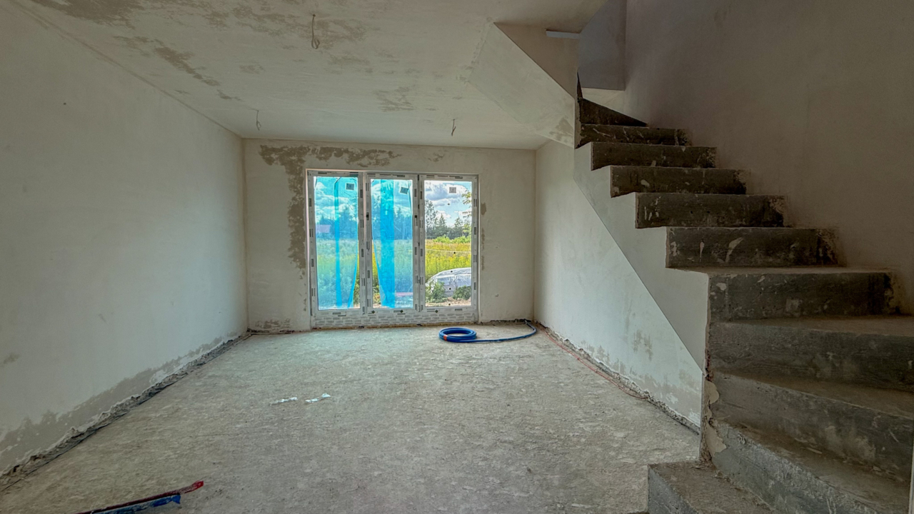 dom w budowie salon z dużym oknem i wyjściem do prywatnego ogrodu oraz schody w rogu salonu