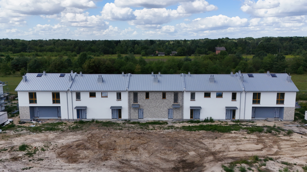 szereg budynków z gotową elewacją na tle lasu i łąki osiedle powstające w sąsiedztwie zieleni